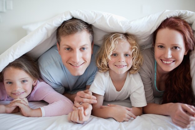 Foto lächelnde familie unter bettdecke