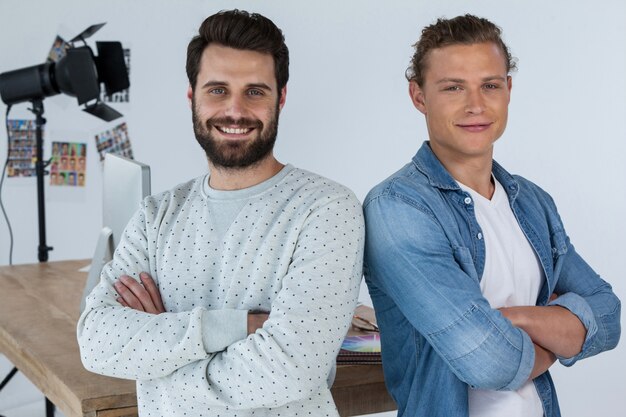 Lächelnde Fotografen, die mit verschränkten Armen im Studio stehen