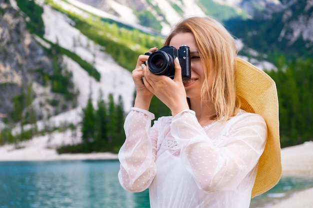 Lächelnde Fotografin mit blonden Haaren und professioneller Kamera, die den See fotografiert