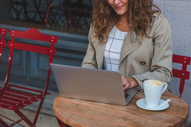 Lächelnde Frau, die am Laptop im Café im Freien arbeitet