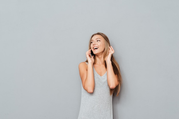 Lächelnde Frau, die am Telefon lokalisiert auf einem grauen Hintergrund spricht