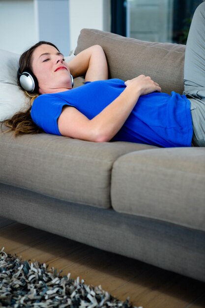 lächelnde Frau, die auf der Couch hört Musik auf ihren Kopfhörern liegt