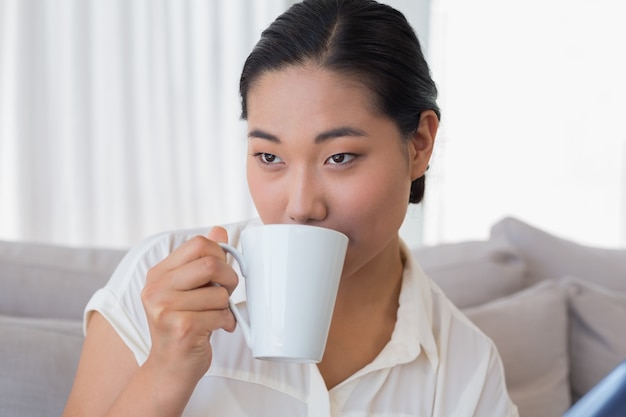 Lächelnde Frau, die auf der Couch trinkt Kaffee sitzt