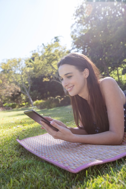 Lächelnde Frau, die auf Matte liegt und digitales Tablett verwendet