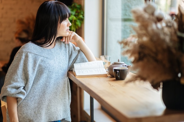 Lächelnde Frau, die Buch am Kaffeehaus liest. Bild der jungen hübschen Frau, die am Tisch im Café sitzt und Buch liest.