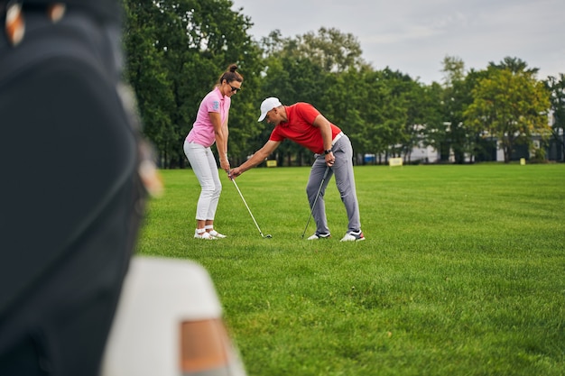 lächelnde Frau, die den richtigen Golfgriff übt, unterstützt von ihrem Trainer