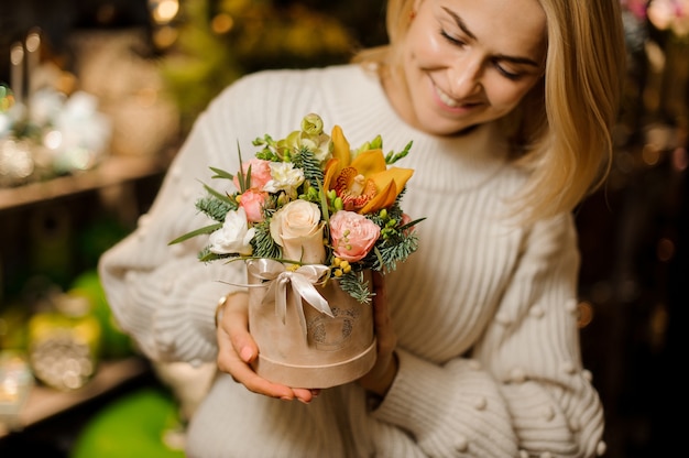 Lächelnde Frau, die eine Pfirsichfarbbox mit rosa Rosen und gelber Orchidee hält