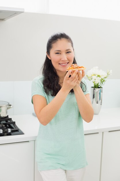 Lächelnde Frau, die eine Scheibe der Pizza in der Küche isst