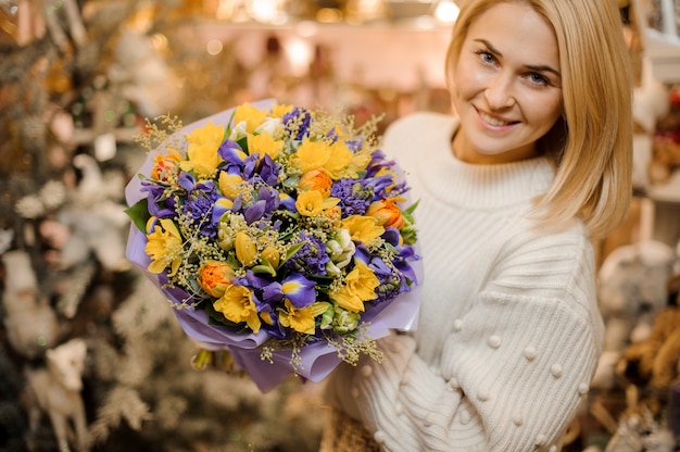 Lächelnde Frau, die einen kleinen Blumenstrauß mit lila und weißen Blumen hält, die in Geschenkpapier eingewickelt werden