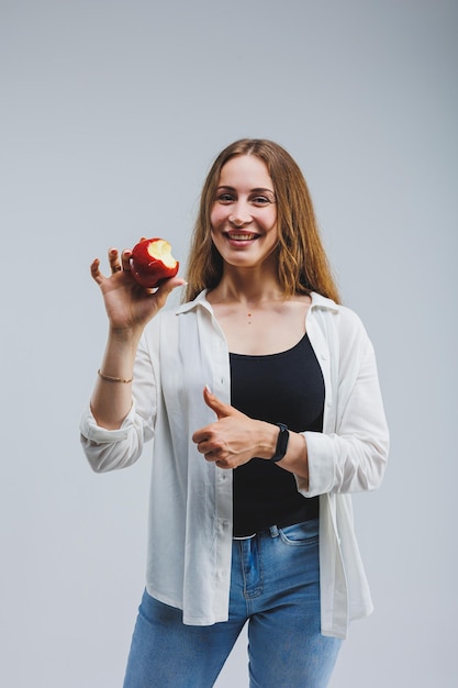 Lächelnde Frau, die einen roten Apfel hält Schöne Brünette in einem weißen Hemd Gesunde Pflanzennahrung und Vitamine Weißer Hintergrund