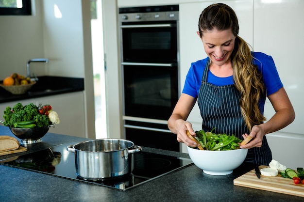 lächelnde Frau, die einen Salat für Abendessen in der Küche wirft