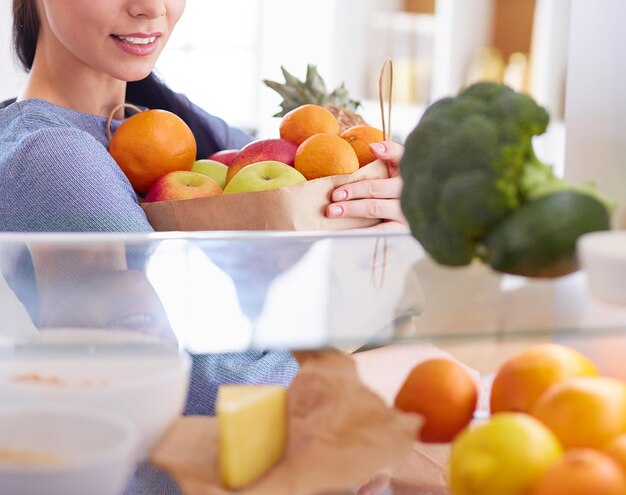 Lächelnde frau, die frisches obst aus dem kühlschrank nimmt, gesundes lebensmittelkonzept