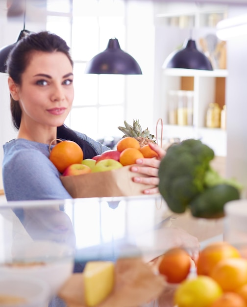 Lächelnde frau, die frisches obst aus dem kühlschrank nimmt, gesundes lebensmittelkonzept