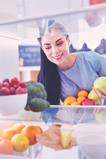 Lächelnde frau, die frisches obst aus dem kühlschrank nimmt, gesundes lebensmittelkonzept