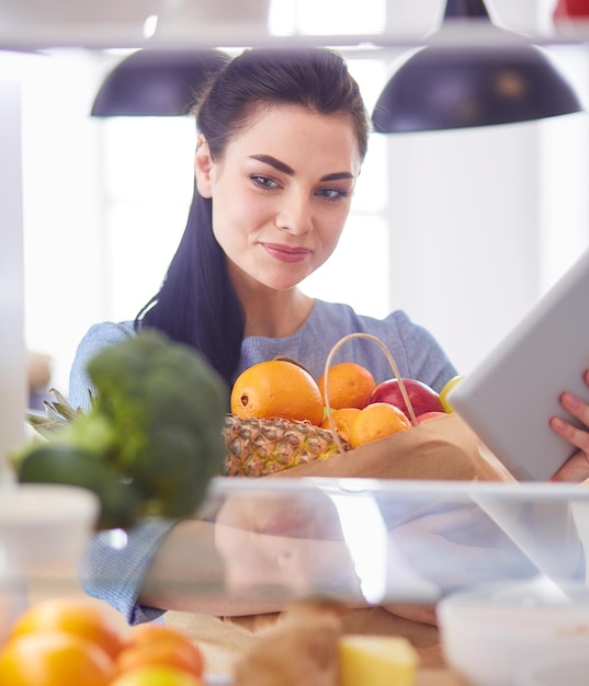 Lächelnde frau, die frisches obst aus dem kühlschrank nimmt, gesundes lebensmittelkonzept