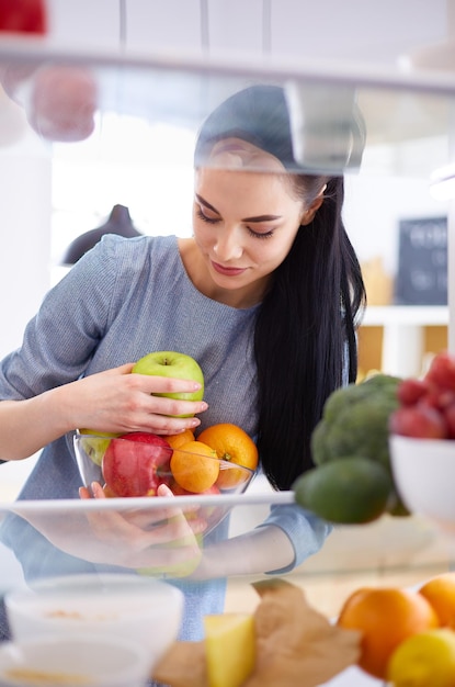 Lächelnde frau, die frisches obst aus dem kühlschrank nimmt, gesundes lebensmittelkonzept