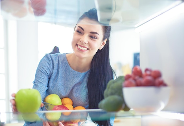 Lächelnde frau, die frisches obst aus dem kühlschrank nimmt, gesundes lebensmittelkonzept