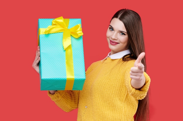 Lächelnde Frau, die Geschenkbox hält und Daumen oben zeigt