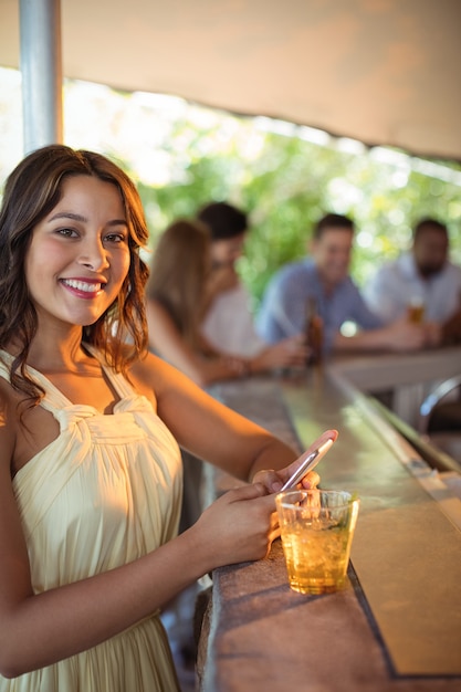 Lächelnde Frau, die Handy benutzt, während sie ein Glas Bier im Restaurant hat