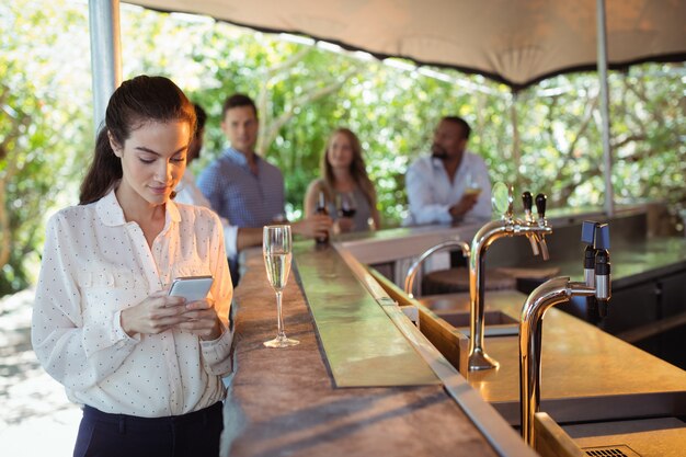 Lächelnde Frau, die Handy benutzt, während sie ein Glas Champagner hat