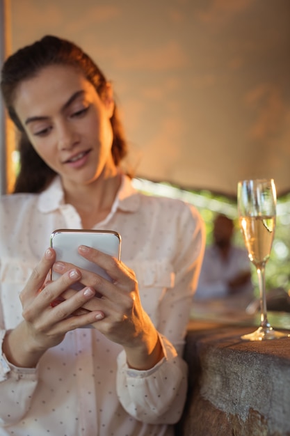 Lächelnde Frau, die Handy benutzt, während sie ein Glas Champagner hat