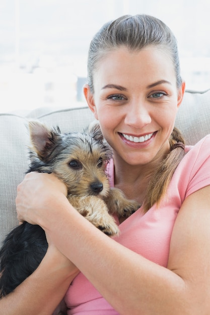 Lächelnde Frau, die ihren Yorkshire-Terrier auf der Couch streichelt