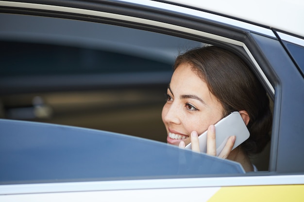 Lächelnde Frau, die im Auto telefonisch spricht