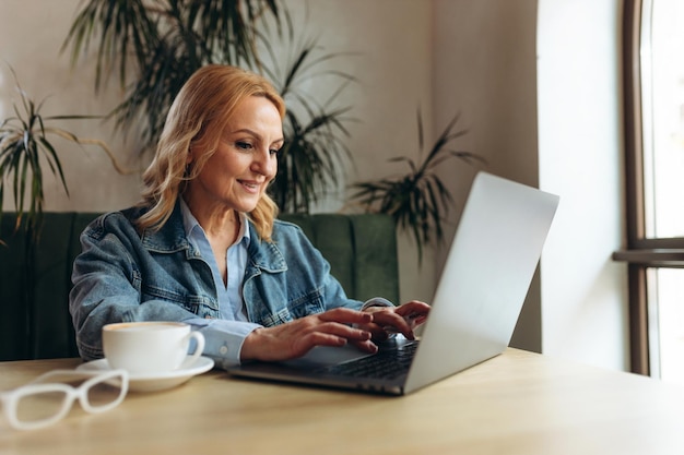 Lächelnde Frau, die in der Cafeteria sitzt, die auf Laptop arbeitet Geschäftsfrau, die E-Mail auf Laptop überprüft Schöne reife Frau und mit Laptop im Café beim Trinken einer Tasse Tee