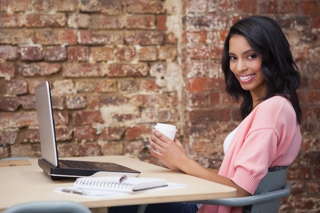 Lächelnde Frau, die Kaffee an ihrem Schreibtisch unter Verwendung des Laptops trinkt