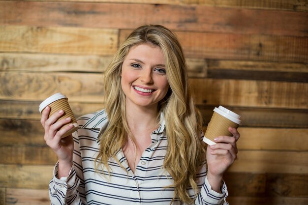 Lächelnde Frau, die mit wegwerfbarer Kaffeetasse im Kaffee steht