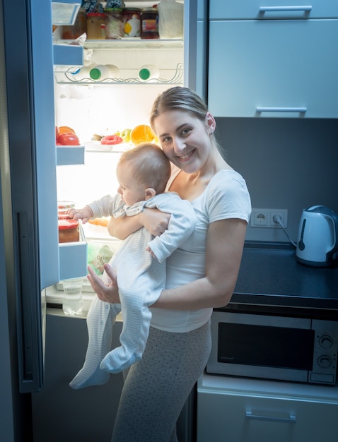 Lächelnde Frau, die nachts mit ihrem kleinen Sohn in der Küche steht