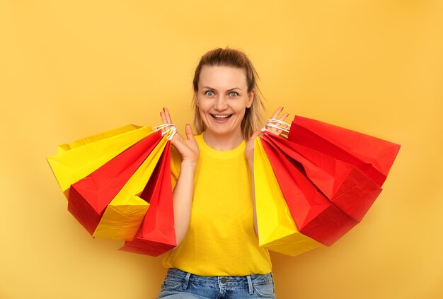 Lächelnde Frau, die Paketbeutel mit Einkäufen lokalisiert auf gelber Wand hält