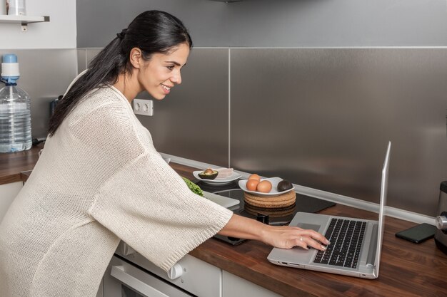 Lächelnde Frau, die Rezept auf Laptop in der Küche wählt