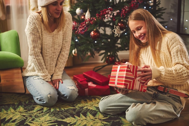 Lächelnde Frau, die Teenager-Tochter am Weihnachtsbaum ein Geschenk gibt