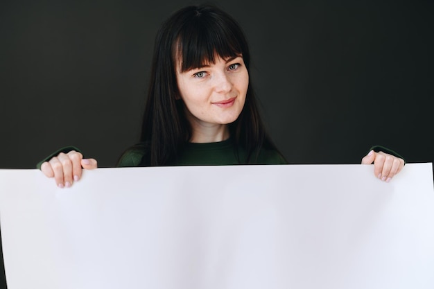 Lächelnde Frau, die weißes Blatt Papier hält Porträt eines Mädchens mit Pony und Sommersprossen auf ihrem Gesicht