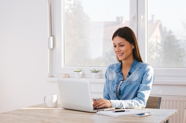 Foto lächelnde frau, die zu hause an laptop arbeitet