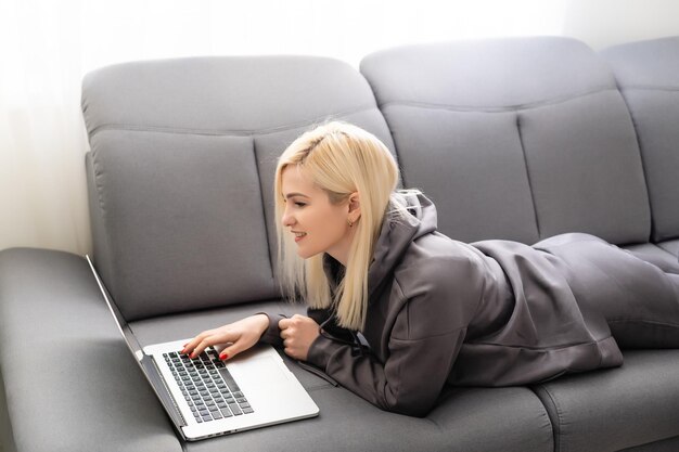 Lächelnde frau, die zu hause auf einem laptop auf einem sofa im internet surft,