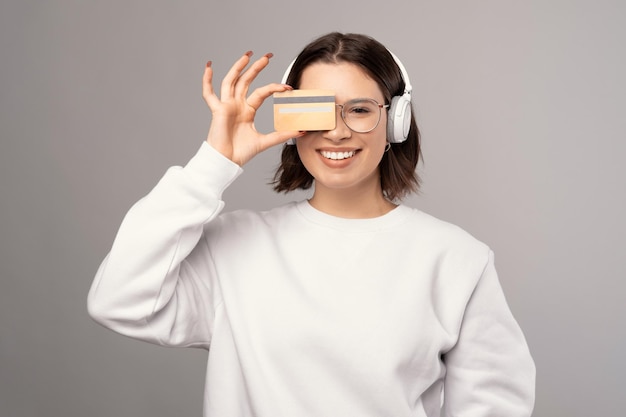 Lächelnde Frau hält eine Kreditkarte und versteckt sich dahinter, während sie Kopfhörer trägt