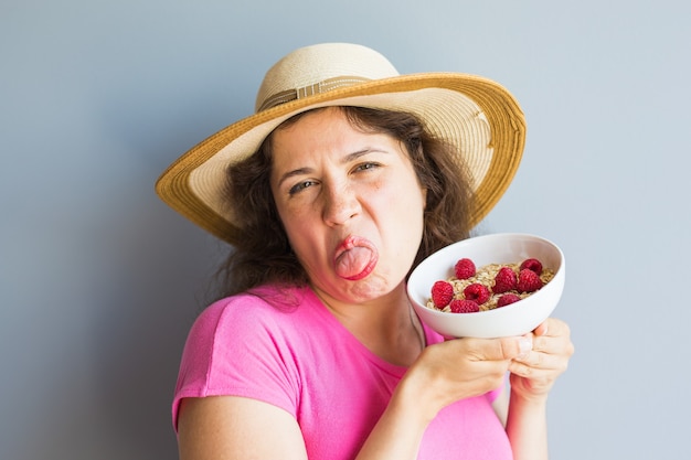 Lächelnde Frau hält gesundes und natürliches Frühstück, Haferflocken und Himbeeren in einer Schüssel.