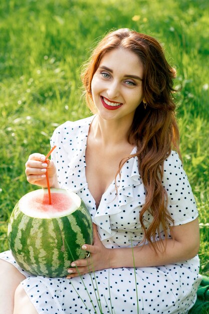 Lächelnde Frau hält Wassermelone mit Cocktailstroh auf Grashintergrund.