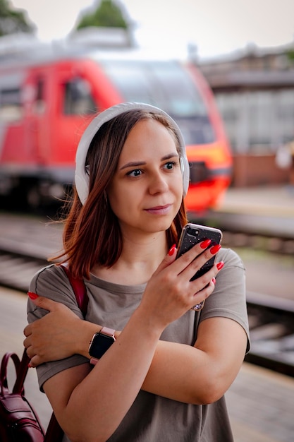 Lächelnde Frau hört Musik mit Kopfhörern mit Smartphone auf Bahnsteig
