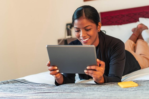 Lächelnde Frau im Bett liegend mit einem digitalen Tablet und Smartphone