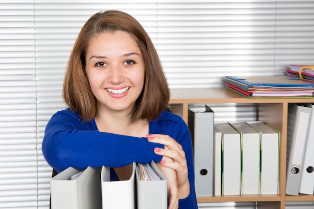 Lächelnde Frau im Büro mit Stapel von Ordnern