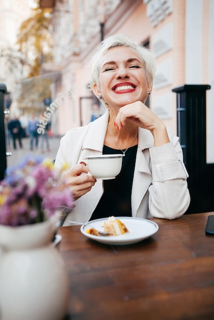 Lächelnde Frau im Café benutzt Smartphone und trinkt Kaffee