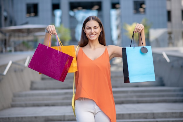 Lächelnde Frau im orangefarbenen Hemd, das Einkaufstasche zeigt