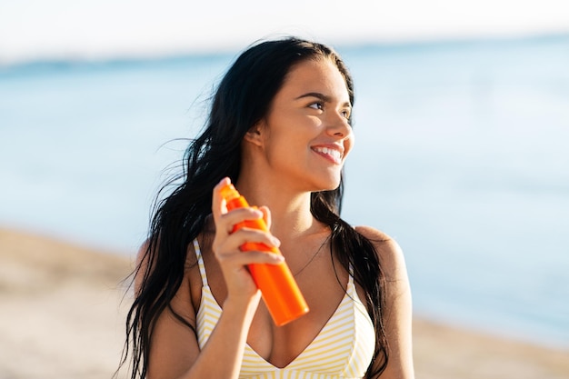 lächelnde Frau in Bikini mit Sonnencreme am Strand