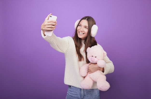 Lächelnde Frau in den Kopfhörern macht selfie mit einem Spielzeugbären