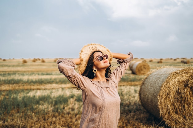 Lächelnde Frau in der Sonnenbrille mit nackten Schultern auf einem Weizenfeld und Heuballen