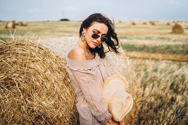 Lächelnde Frau in der Sonnenbrille mit nackten Schultern auf einem Weizenfeld und Heuballen
