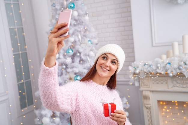 Lächelnde Frau in einem Pullover und Hut, die ein Selfie auf einem Smartphone nehmen